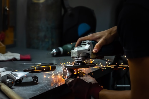 Männlicher Metallarbeiter poliert und finalisiert ein Stück mittelalterlichen Rüstungsanzugs. Mannhände, die Metallteile der Hardware in einer Werkstatt mit Winkelschleifer behandeln.