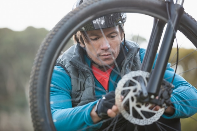 Foto männlicher mountainbiker, der vorderrad seines fahrrads untersucht