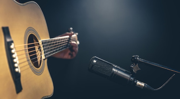 Männlicher Musiker, der Akustikgitarre hinter dem Mikrofon im Aufnahmestudio spielt