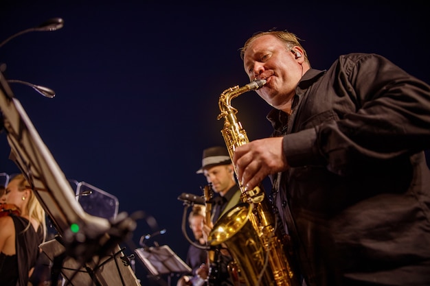 Männlicher Musiker, der Saxophon unter blauem Nachthimmel spielt