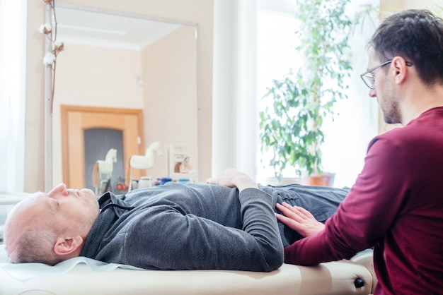 Männlicher Patient, der eine kraniale Sakraltherapie erhält und auf dem Massagetisch in der CST-Klinik für Osteopathie, Osteopathie und manuelle Therapie liegt