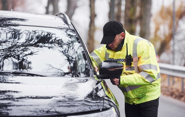 Männlicher Polizist in grüner Uniform, der das Fahrzeug auf der Straße überprüft.