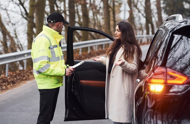 Männlicher Polizist in grüner Uniform im Gespräch mit der Besitzerin des Autos auf der Straße.