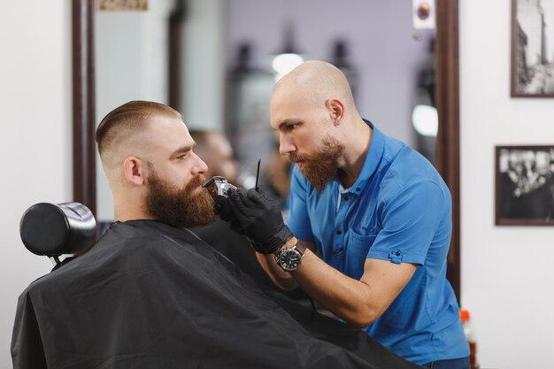 Männlicher professioneller Friseur, der Kunden bedient und dicke, große Bartrasierer rasiert