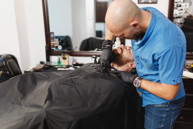 Männlicher professioneller Friseur, der Kunden bedient und dicke, große Bartrasierer rasiert