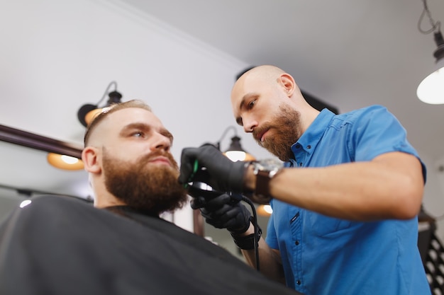 Männlicher professioneller Friseur, der Kunden mit Schermaschine bedient