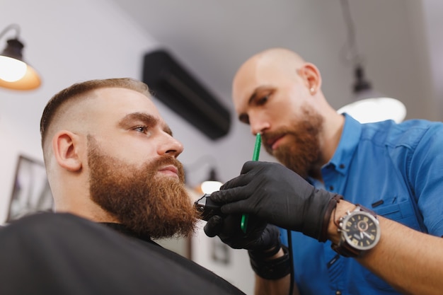 Männlicher professioneller Friseur, der Kunden mit Schermaschine bedient