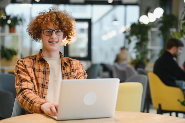 Männlicher Programmierer trägt eine Brille zum Schutz der Augen, während er freiberuflich über einen Laptop arbeitet, der sich ein Tutorial auf einem Netbook ansieht