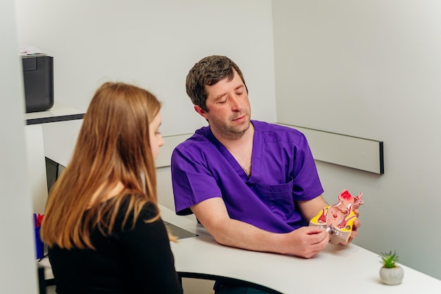 Männlicher Proktologe, der dem Patienten im Krankenhaus während der Konsultation ein künstliches Modell des menschlichen Rektums zeigt