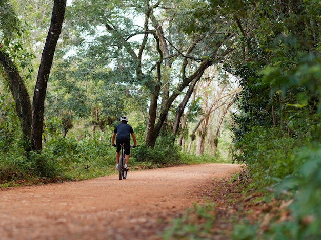 Männlicher Radfahrer reitet Landstraßen im Dschungel. Tropisches Klima. Rückansicht.