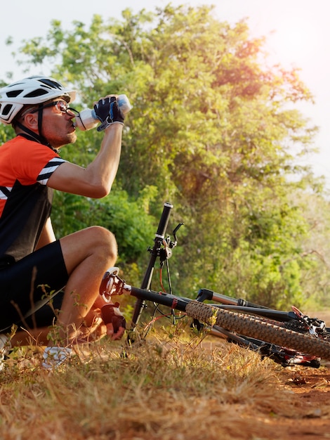 Männlicher Radfahrer sitzt in der Nähe eines Fahrrads trinkt Wasser