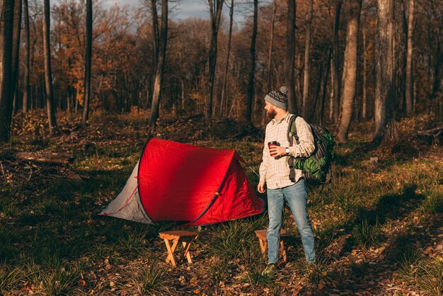 Foto männlicher reisender mit getränk zum mitnehmen und rucksack auf dem campingplatz