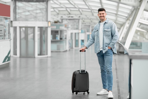 Männlicher Reisender posiert mit Koffergepäck und steht drinnen am Flughafen