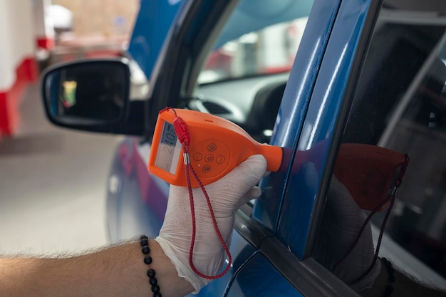 Männlicher Reparaturarbeiter, der Autolack mit Ausrüstung in der Werkstatt untersucht