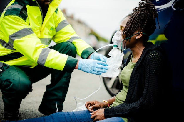 Männlicher Sanitäter, der einer verletzten Frau auf einer Straße eine Sauerstoffmaske aufsetzt