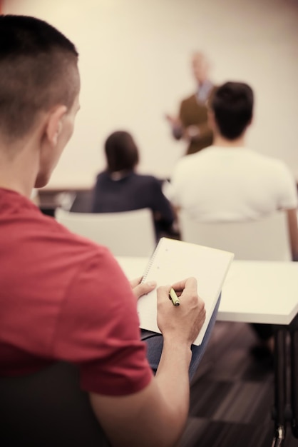 Foto männlicher schüler, der sich im klassenzimmer notizen macht. betriebswirtschaftliches bildungskonzept, lässiger junger geschäftsmann im seminartraining