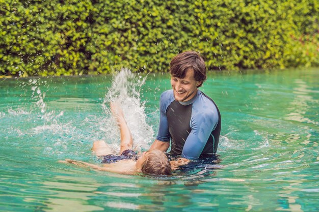 Männlicher Schwimmlehrer für Kinder bringt einem glücklichen Jungen bei, im Pool zu schwimmen