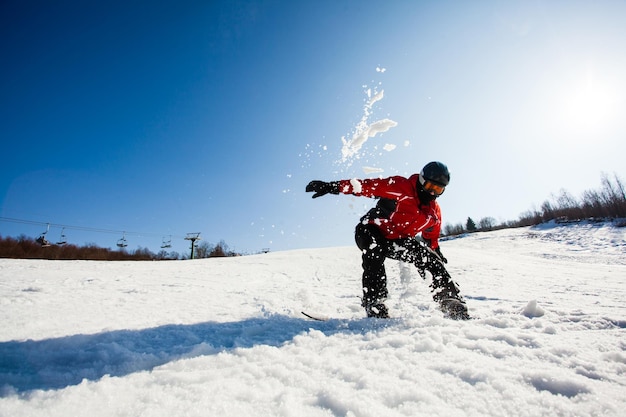 Männlicher Snowboarder in der Momemt des Herunterfallens auf dem Schnee Schneewolke über dem Kopf Blauer Himmel mit heller Sonne auf einem Hintergrund