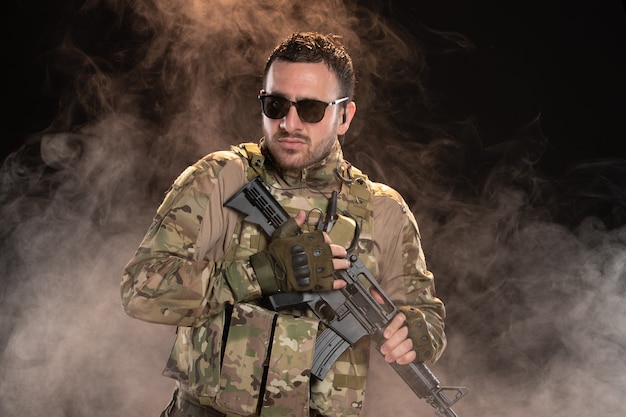 Männlicher Soldat in Tarnung mit Maschinengewehr an dunkler Wand