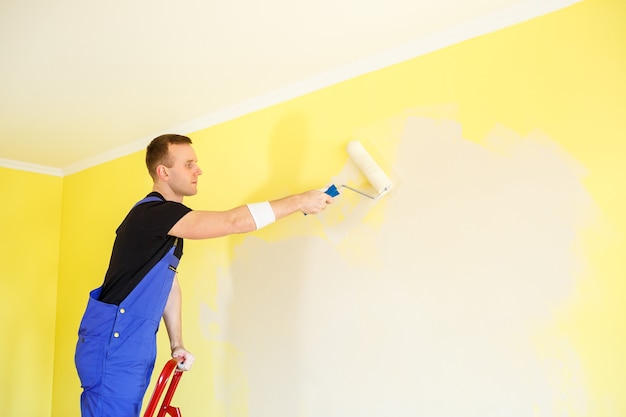 Männlicher Spezialist streicht die Wand mit Farbe im Innenbereich, Reparaturkonzept