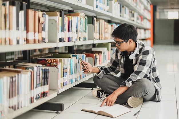 Männlicher Student arbeitet an Aufgaben und surft mit dem Smartphone, während er Bücher öffnet