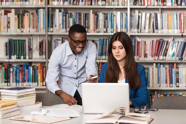 Männlicher Student, der am College lacht Hübsche zwei College-Studenten mit Laptop und Büchern, die in einer High School-Universitätsbibliothek arbeiten Geringe Schärfentiefe