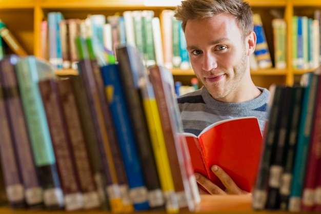 Männlicher Student, der ein Buch in der Bibliothek liest