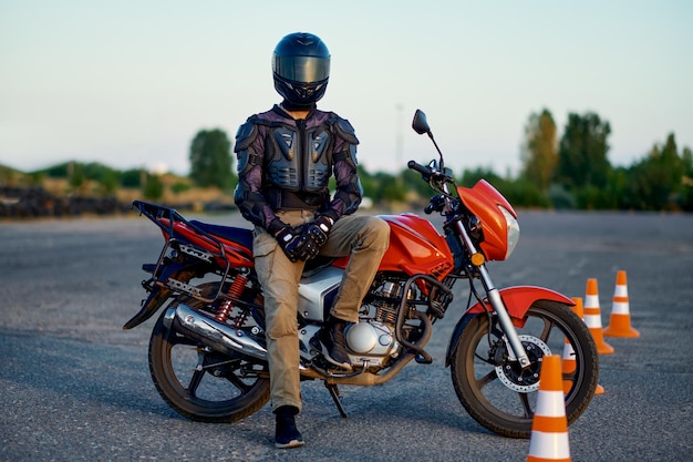 Männlicher Student posiert auf dem Motorrad und fährt auf dem Motodrome in der Motorradschule. Ausbildung von Motorradfahrer-Anfängern, Biker-Übungen in der Motorschule