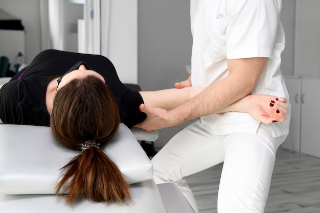 Männlicher Therapeut, der einer Patientin in der Physiotherapieklinik Massage zur Linderung von Schulterschmerzen gibt.