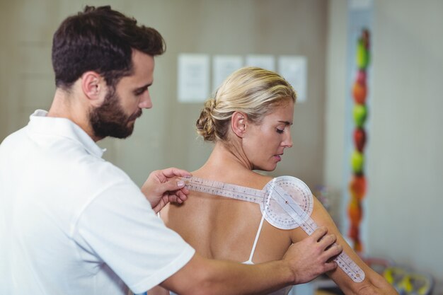 Foto männlicher therapeut, der weiblichen patienten zurück mit goniometer misst