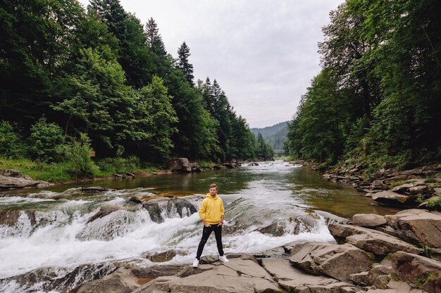 Männlicher Tourist steht an der frischen Luft im Wald am Bergfluss