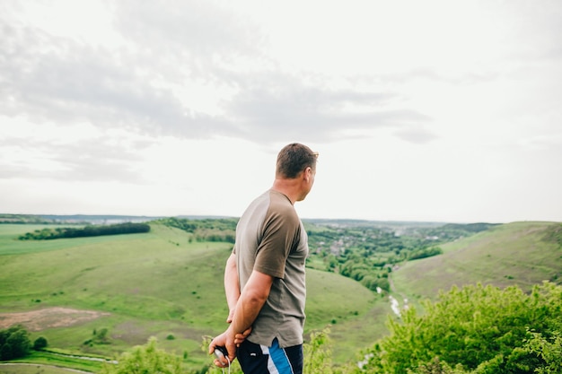Männlicher Tourist steht auf einem Klippenhügel und betrachtet die grüne Landschaft des Flusses und des Tals