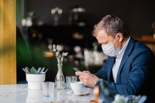 Männlicher Unternehmer trägt während des Ausbruchs des Coronavirus eine medizinische Maske und sitzt im Café