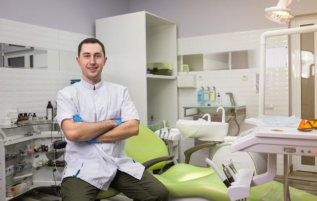 Männlicher Zahnarzt, der mit gekreuzten Händen über dem Hintergrund des medizinischen Büros steht Gesundheitsberuf Stomatologie und Medizinkonzept