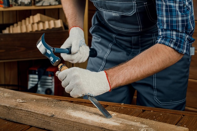 Männlicher Zimmermann hämmert Holz mit einem Meißel. Zimmermannswerkzeuge.