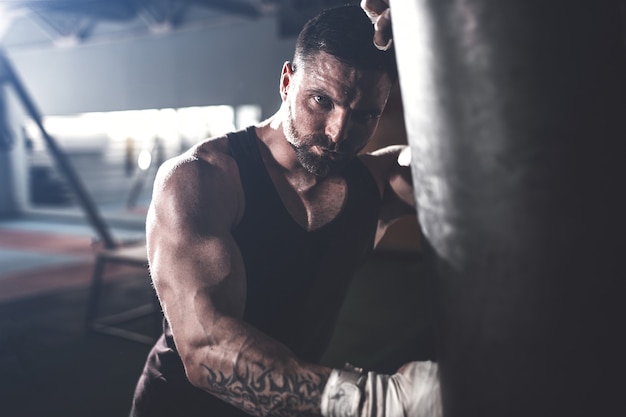 Männliches Boxertraining mit Sandsack in der dunklen Sporthalle.