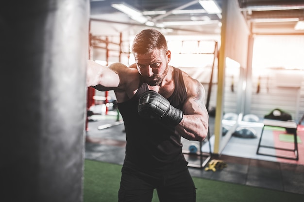 Männliches Boxertraining mit Sandsack in der dunklen Sporthalle.