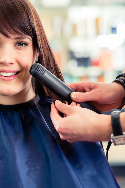 Männliches coiffeur Kleidfrauenhaar mit flachem Eisen im Shop