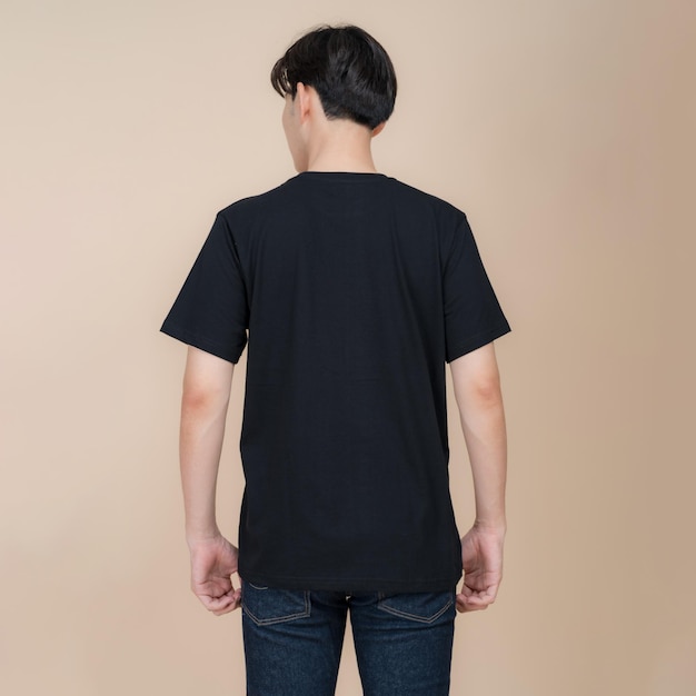 Männliches Model in schwarzem T-Shirt und Jeans steht im Studio auf beigem Hintergrund