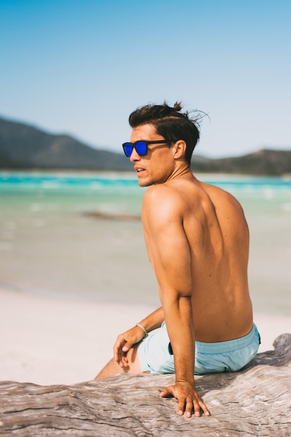 Männliches Modell, das Sonnenbrille und Fitnesskörper auf der Strandaufstellung trägt