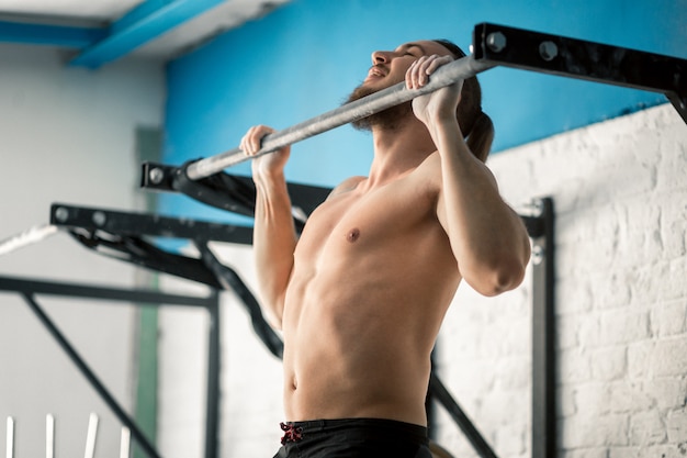 Männliches Modell der muskulösen Fitness des Athleten, das an der horizontalen Stange in einer Turnhalle hochzieht