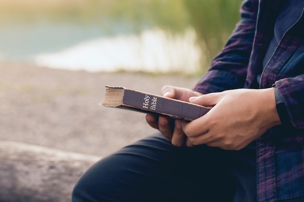 Männliches Sitzen und Halten der Bibel in den Händen mit Naturhintergrund. Sonntagslesungen, Bibel