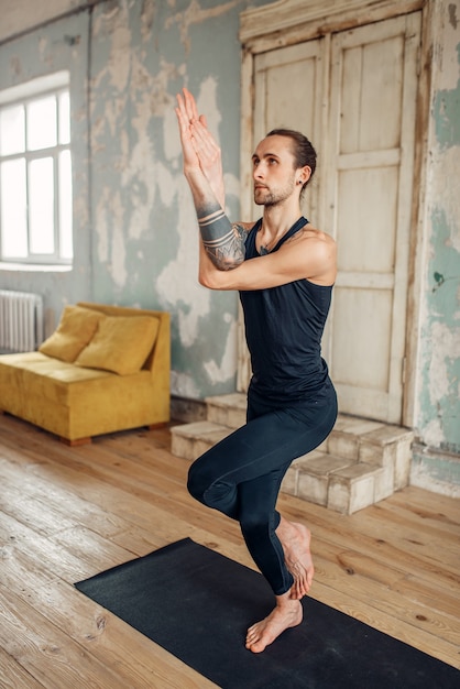 Männliches Yoga, das Gleichgewichtsübung auf Matte im Fitnessstudio tut