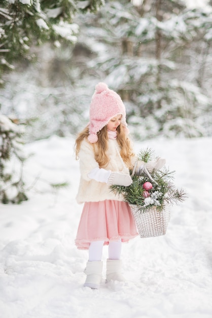 Märchen ein schönes Mädchen in einem weißen Pelzmantel mit einem weißen großen Korb mit Tannenzweigen in einem schneebedeckten Wald des Winters.