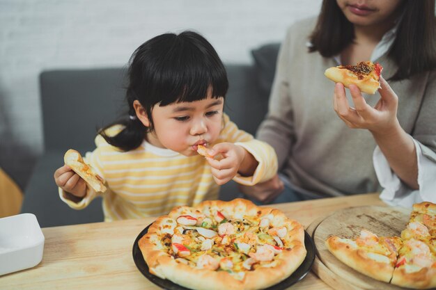 Mães e crianças asiáticas fazem atividades em casa mãe vai alimentar pizza para seus filhos