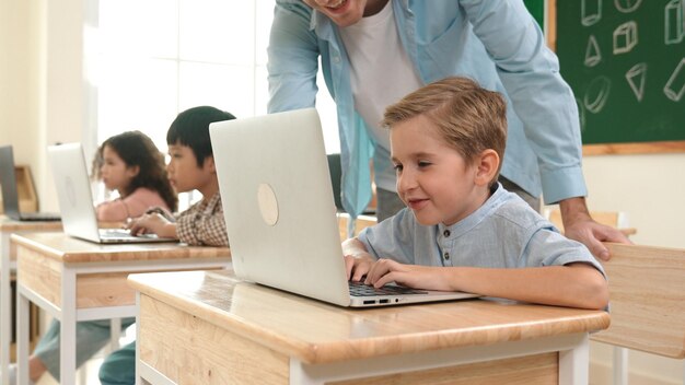 Maestra caucásica ayudando a un niño enérgico a codificar ingeniería pedagogía rápida