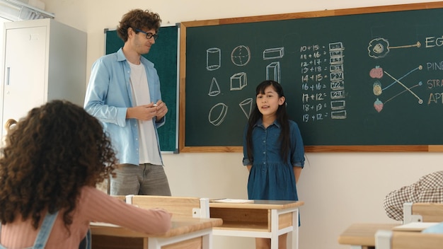 Maestra caucásica mirando a un estudiante que se presenta en la pizarra de pedagogía