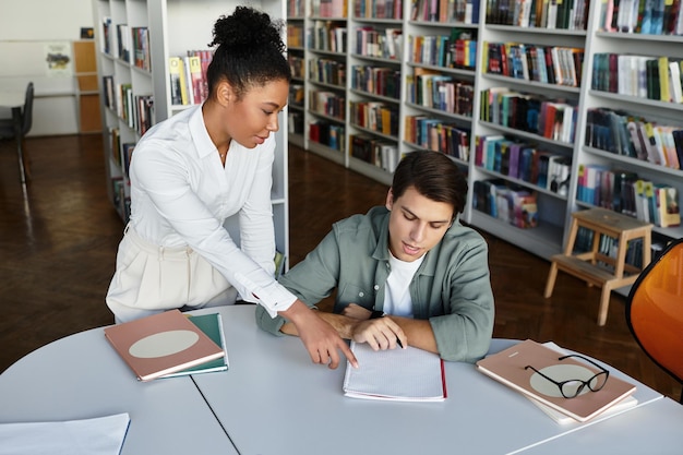 Una maestra dedicada guiando a su estudiante ansioso a través de las lecciones en un entorno de biblioteca