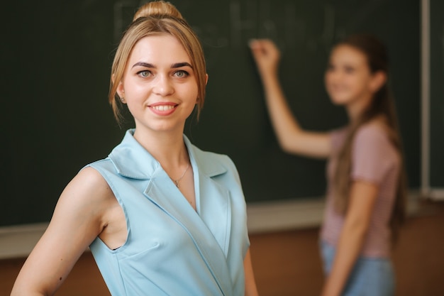 Maestra delante de la colegiala escribiendo algo en la pizarra en el aula