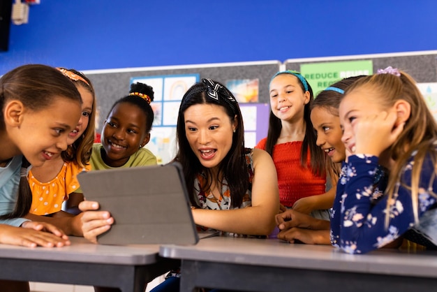 Foto maestra diversa con tableta y alumnas de primaria en la clase